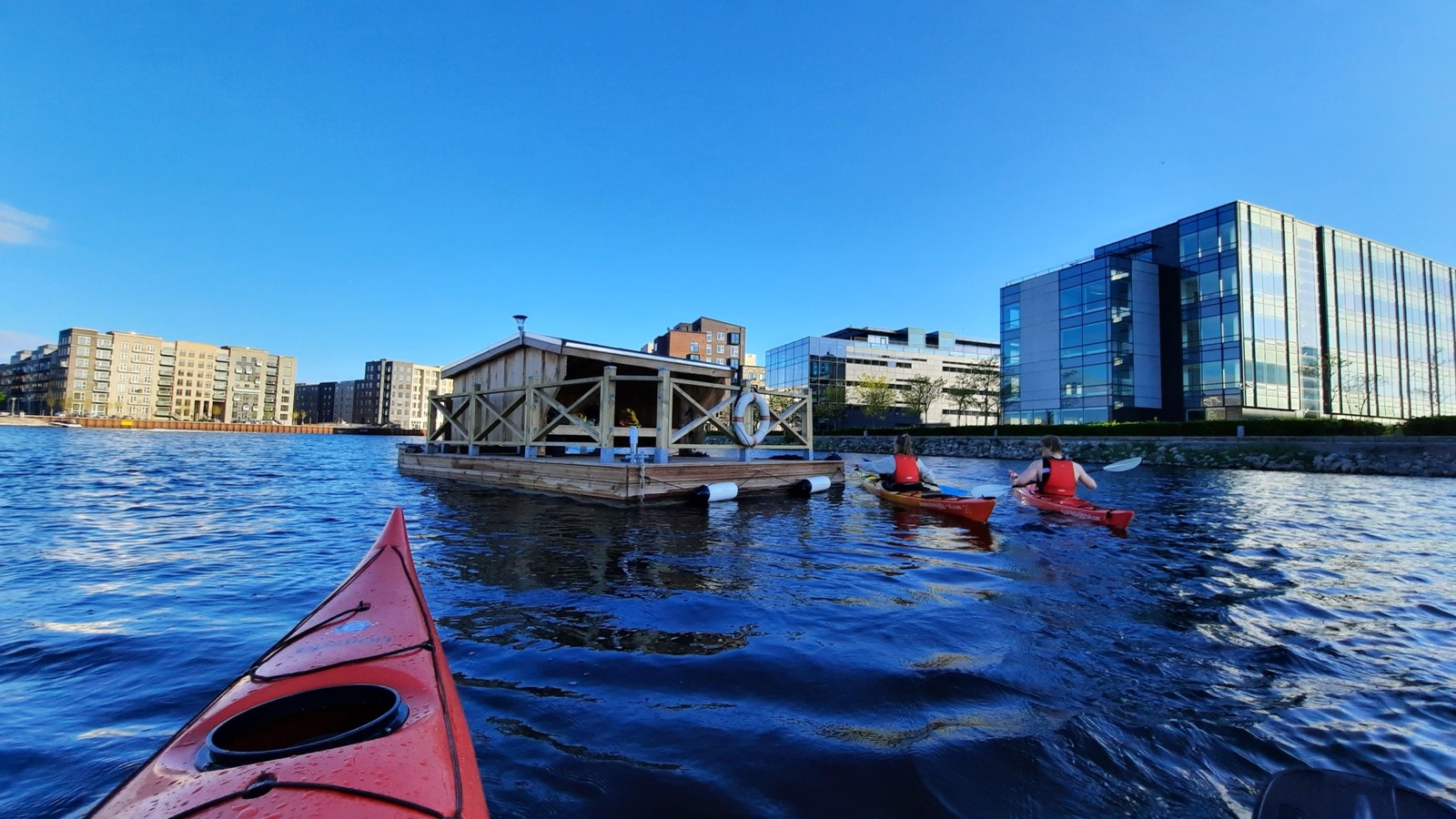 En kajak padler mod en flydende shelter i havnen